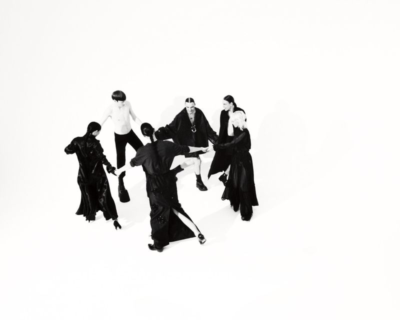 Group of seven fashionably dressed people in black and white, standing in a circle on a white background, overhead shot, minimal.