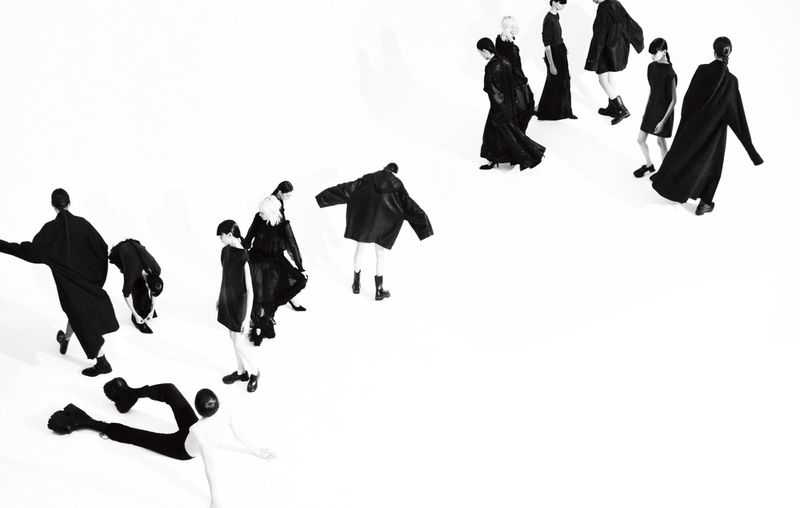 Group of models in black clothing pose against a white background, showcasing fashion and design with a high-angle, studio shot.