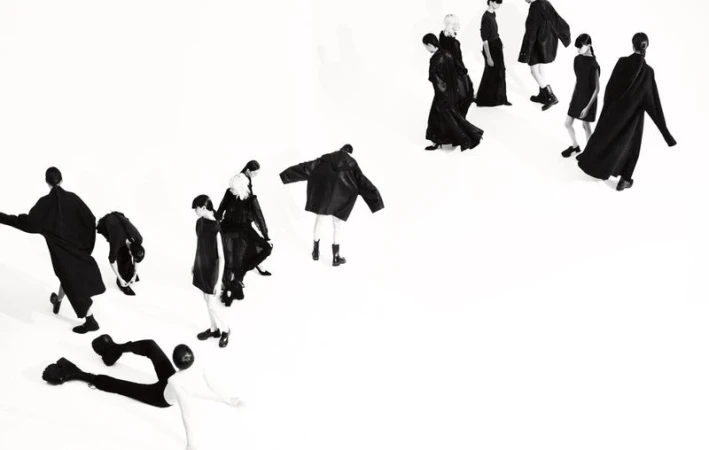Group of models in black clothing pose against a white background, showcasing fashion and design with a high-angle, studio shot.