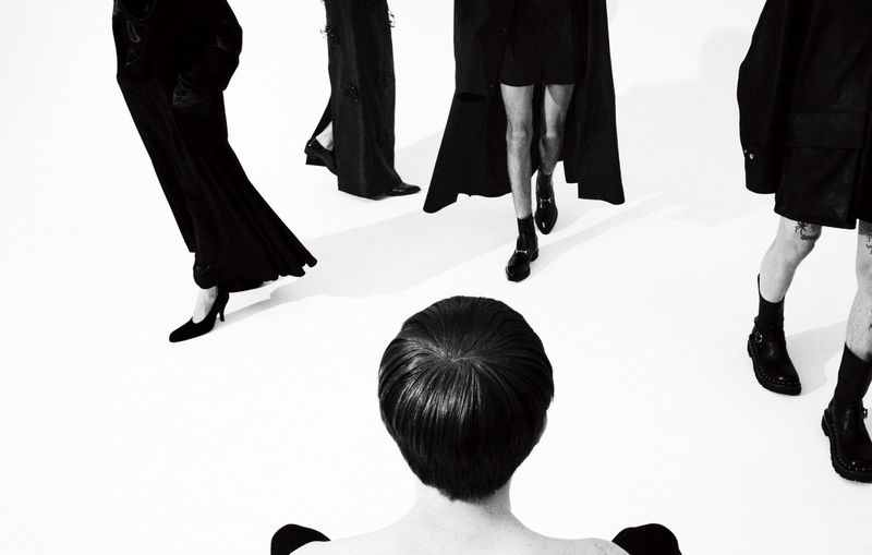 Black and white fashion shot featuring a group of androgynous models wearing dark clothing against a seamless white backdrop.