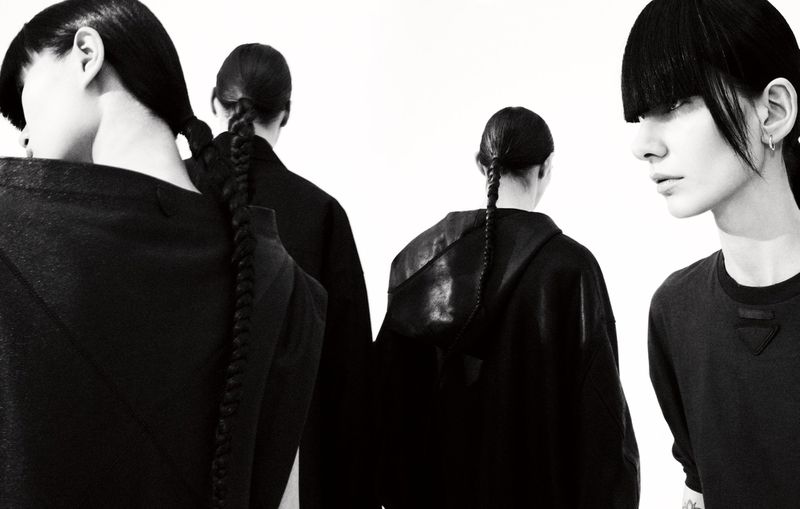 High-contrast studio shot of four women with black hair in braids and modern black outfits against a clean white backdrop.