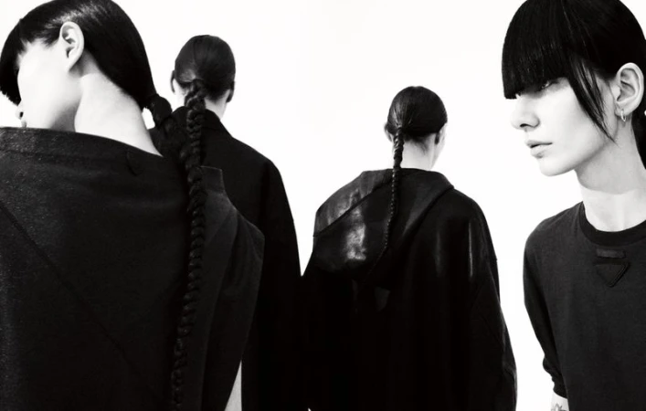 High-contrast studio shot of four women with black hair in braids and modern black outfits against a clean white backdrop.