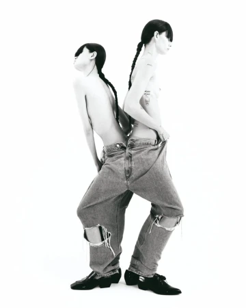 Two shirtless adults in ripped denim stand back-to-back against a white backdrop, showcasing a minimalist fashion concept.