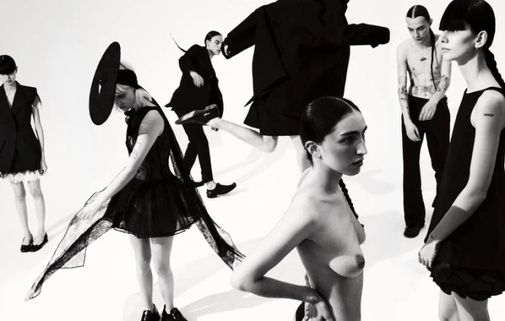 Fashion editorial shot of six slender models in a stark studio setting showcasing avant-garde black clothing, striking poses in a high-contrast black and white aesthetic.