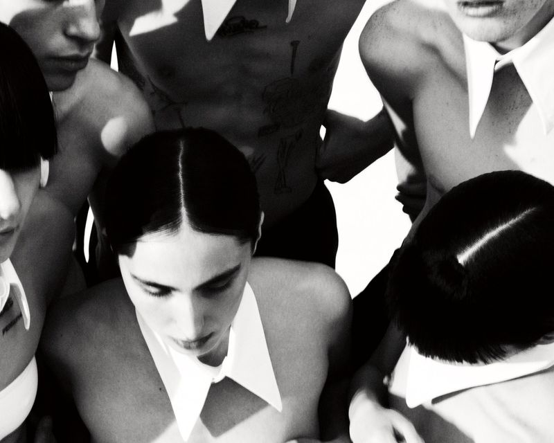 Group of young adults wearing white collars, set against a bright backdrop in a black and white studio-style photograph.