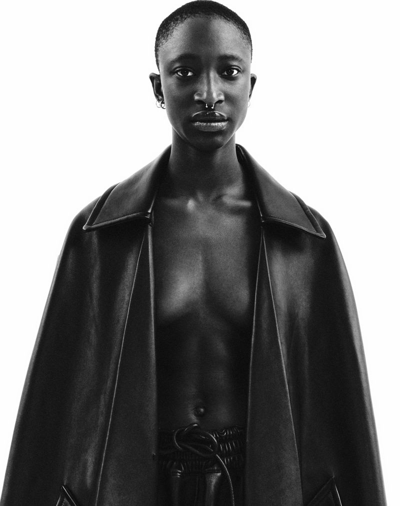Striking portrait of a Black adult female wearing a black leather jacket, posing in a photo studio with a bright white background.