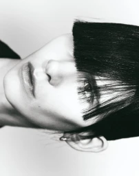 Close-up portrait of a model with blunt bangs and dark hair against a white background for Boycott Magazine
