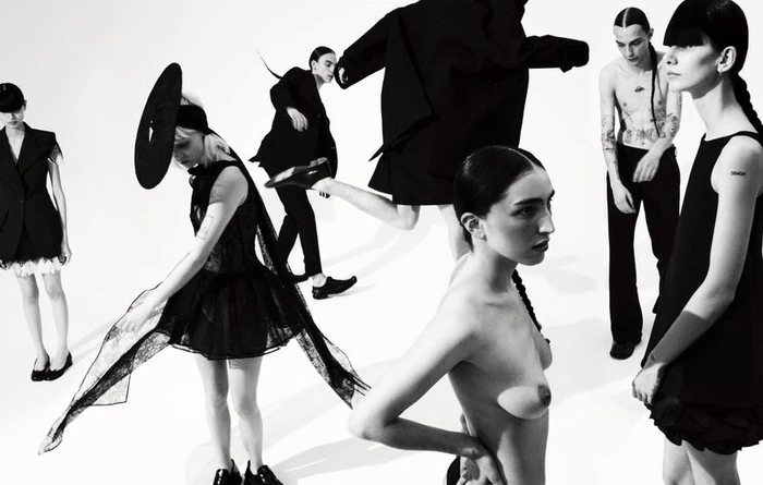 Monochrome fashion editorial image featuring multiple models in dark clothing against a bright white background.