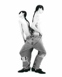 Two models back to back wearing oversized distressed denim jeans and black shoes against a plain white background.