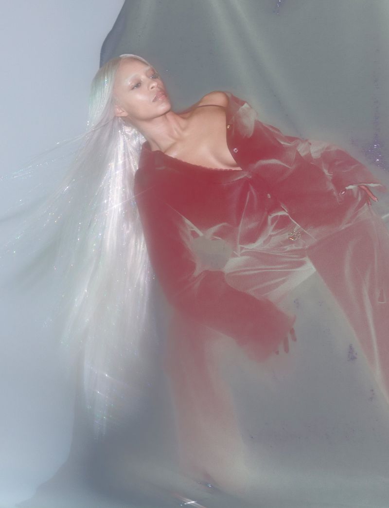 Woman in red jacket and silver wig lying down against a light gray background with soft lighting. Fashion, beauty, and creative concept.