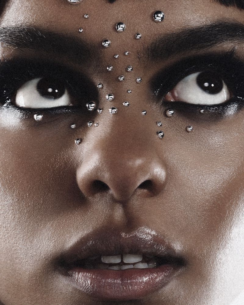 Close-up portrait of a woman with dark eye makeup and metallic studs on her face looking upward for Numero Netherlands