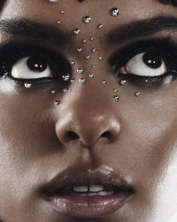 Close-up portrait of a woman with dark eye makeup and metallic studs on her face looking upward for Numero Netherlands
