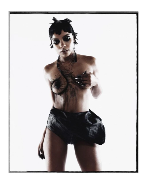 Artistic studio shot of a woman in minimal black attire, featuring unique hair and nail design, against a stark white backdrop.