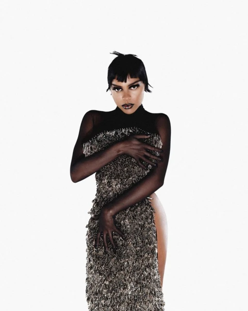 Woman in fringed dress poses in a fashion-forward portrait against a clean white background, showcasing the garment's unique texture and design.