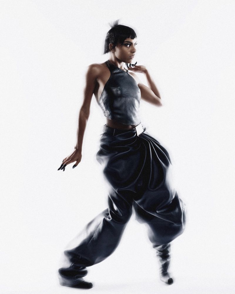 Model in a black halter top and dark trousers posing against a bright white background for Numero Netherlands.