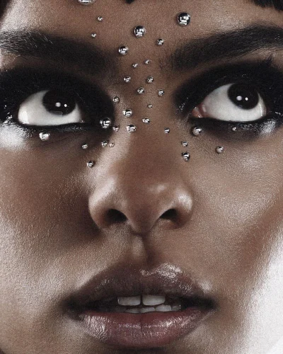 Close-up portrait of a woman with dark eye makeup and metallic studs on her face looking upward for Numero Netherlands