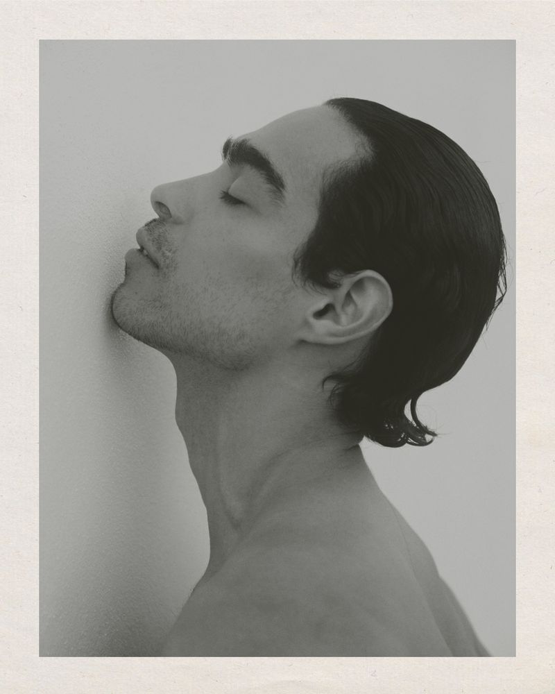 Monochrome portrait of a bare-chested man with his eyes closed, head leaning against a wall, captured in a studio setting.
