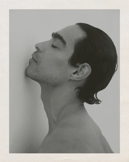 Monochrome portrait of a bare-chested man with his eyes closed, head leaning against a wall, captured in a studio setting.