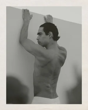 Monochrome portrait of a shirtless man gripping a high wall from behind