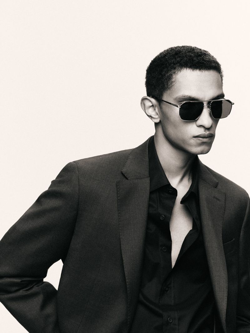 Close-up studio shot of a stylish adult male in a dark suit and sunglasses, posing against a neutral backdrop. Fashion editorial.