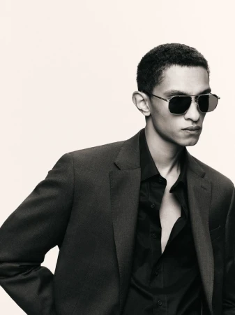 Close-up studio shot of a stylish adult male in a dark suit and sunglasses, posing against a neutral backdrop. Fashion editorial.