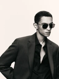 Model wearing a dark blazer, black shirt, and sunglasses against a plain off-white background