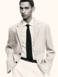 Man wearing a light suit jacket over a striped shirt and dark tie against a white background