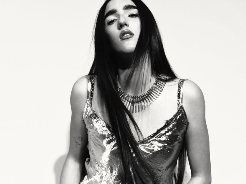 Black and white portrait of a woman wearing a metallic strapless top and statement spike necklace against a white background.