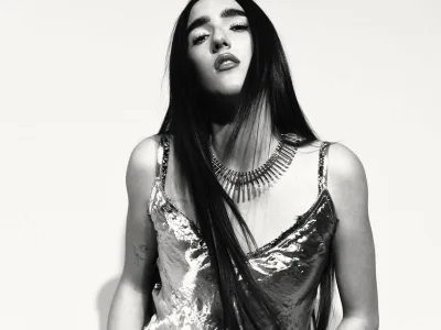 Black and white portrait of a woman wearing a metallic strapless top and statement spike necklace against a white background.