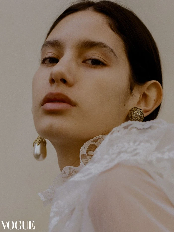 Close-up fashion portrait of a model wearing ornate pearl drop earrings and a white lace collar