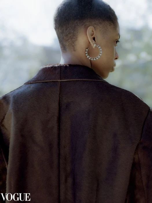 Close-up portrait of a model with short textured hair wearing large hoop earrings and a dark textured coat for Vogue.it