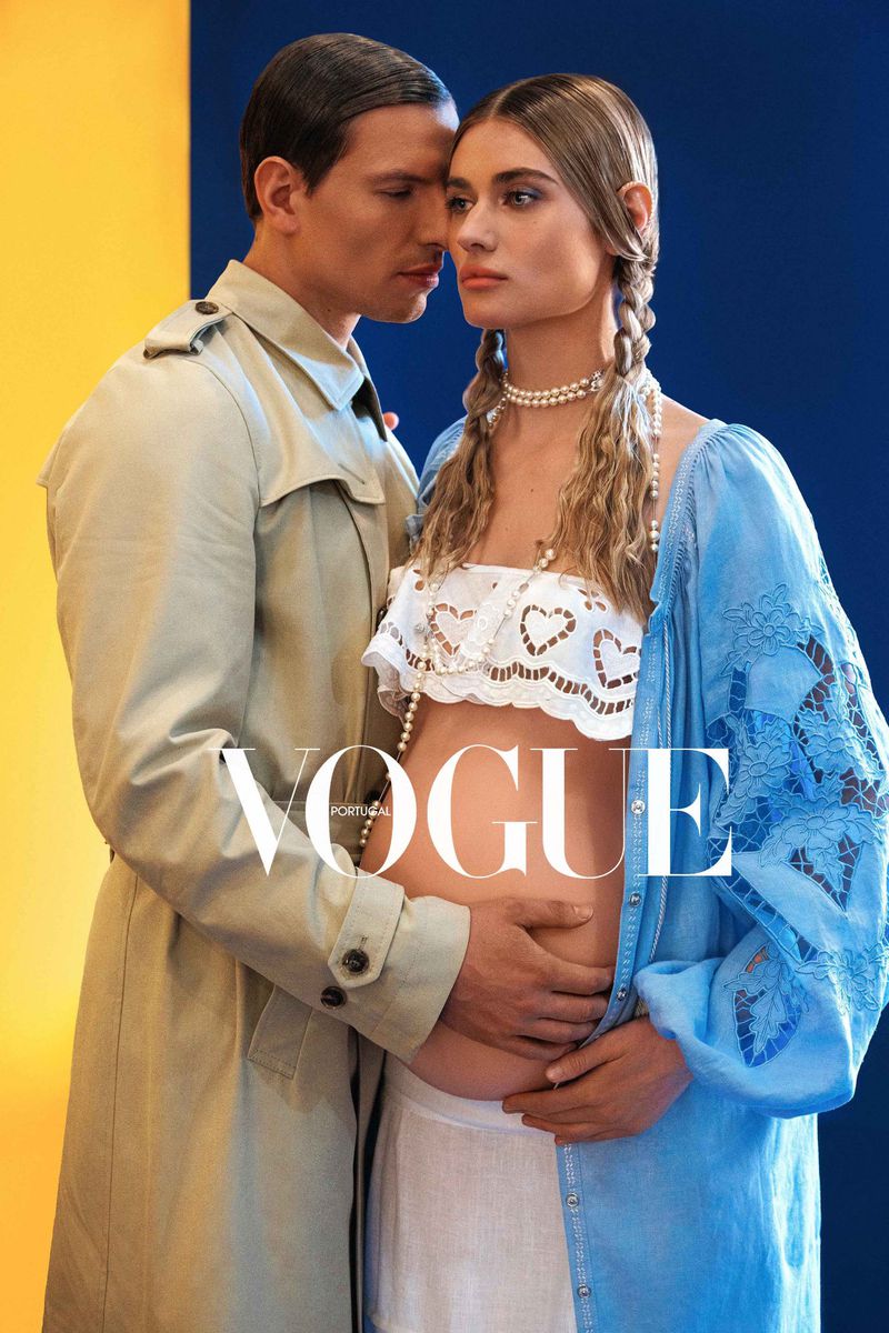 Vogue magazine cover featuring a fashion photo of a pregnant woman in a white top and blue dress posing with a man in a trench coat.