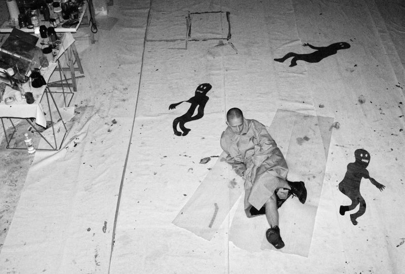 Monochrome shot of an artist sitting amid his black silhouette artwork on a large white canvas in a bright artist's studio.