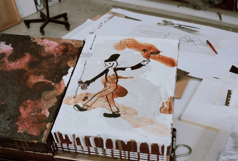 Whimsical character art on display in an artist's studio, featuring a vintage cartoon figure, painted on a block with visible brushstrokes and brown drips.