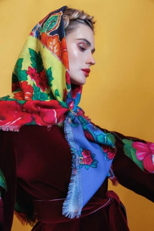 Woman wearing a vibrant floral headscarf and dark red velvet dress against a yellow background for Vogue Portugal Silhuetas de esperança