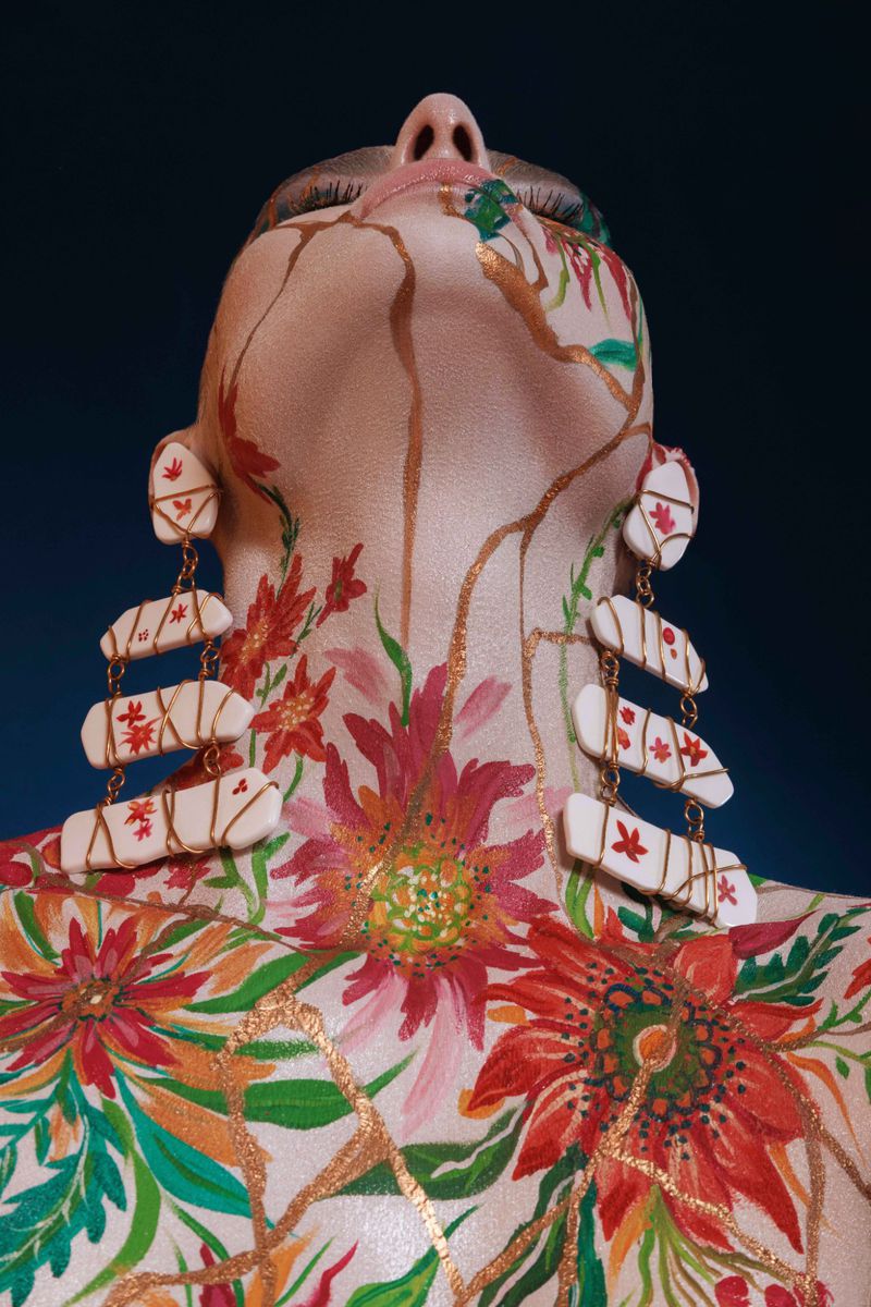 Person with body art. Woman painted with red and green floral pattern and gold accents. Artistic, creative beauty shot on dark background.