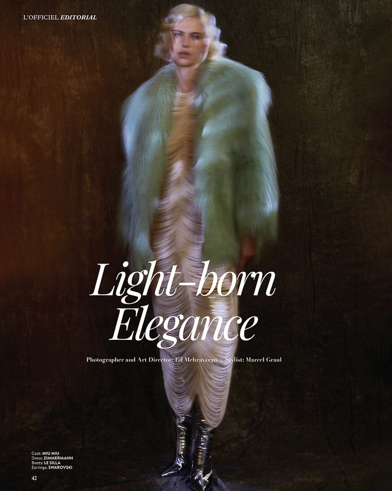 Fashion editorial shot of a person with fair skin, wearing a mint fur coat, dress and reflective boots, posing against a textured background.