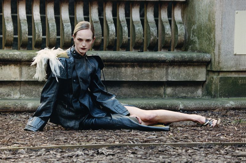 Model Jean Campbell in a dark leather jacket seated outdoors on stone and mulch for W Magazine China