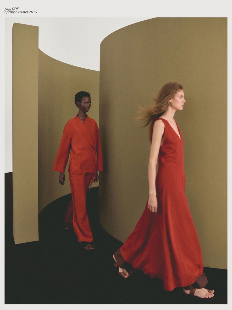 Two fashion models in red dresses walk in an abstract studio setting with muted colors and geometric shapes, fashion editorial photography.