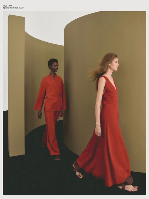 Two fashion models in red dresses walk in an abstract studio setting with muted colors and geometric shapes, fashion editorial photography.