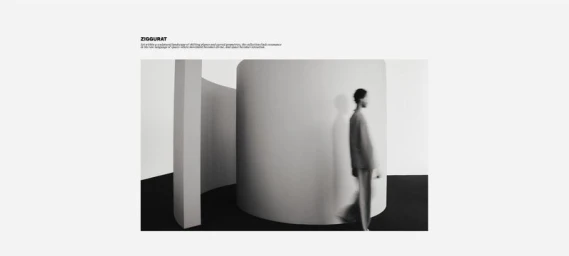 Monochrome fashion editorial image of a model in motion walking past minimalist curved architectural structures.