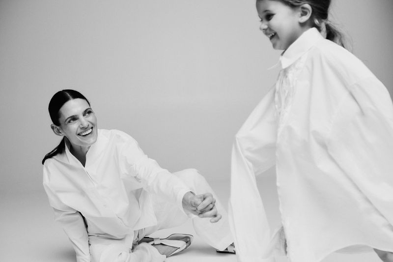Black and white portrait of a smiling adult woman holding hands with a smiling child in an indoor setting, both wearing white shirts.