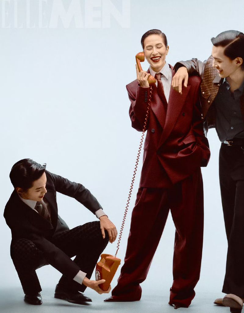Three asian adult male models in suits pose with a vintage telephone in a studio setting, highlighting retro fashion and communication.