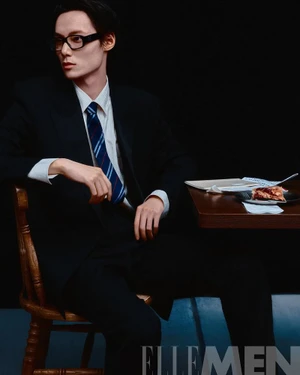 Man wearing a dark suit, striped tie, and glasses seated at a wooden table with a slice of pie for Elle Men China.