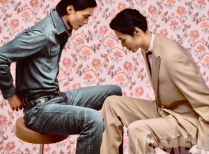 Two male models in styled apparel posed closely together against a pink floral patterned wallpaper backdrop for Elle Men China.