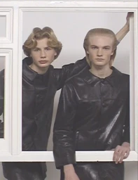 Two young male models wearing dark leather jackets posing inside a white window frame structure for Fantastic Man editorial.