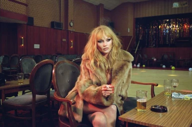 Kate Moss seated at a table in a pub wearing a fur coat for The Perfect Magazine editorial