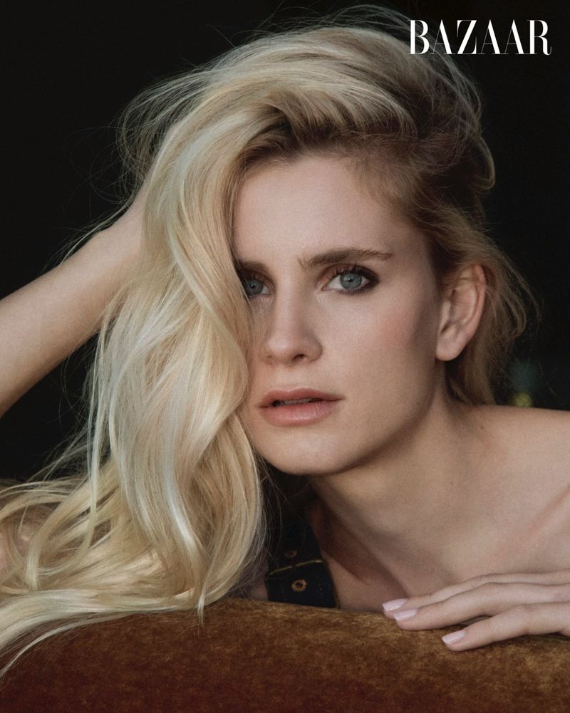 Close-up portrait of a blonde woman with blue eyes resting her hand in her hair against a dark background for Harper's Bazaar China.