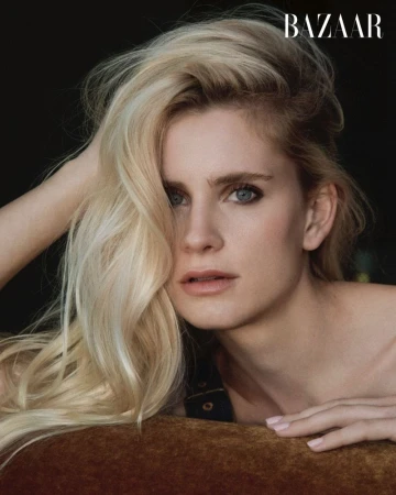 Close-up portrait of a blonde woman with blue eyes resting her hand in her hair against a dark background for Harper's Bazaar China.