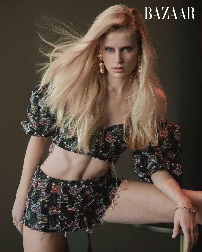 Blonde model poses indoors wearing a two-piece black embellished crop top and skirt, along with gold jewelry and BAZAAR magazine logo.